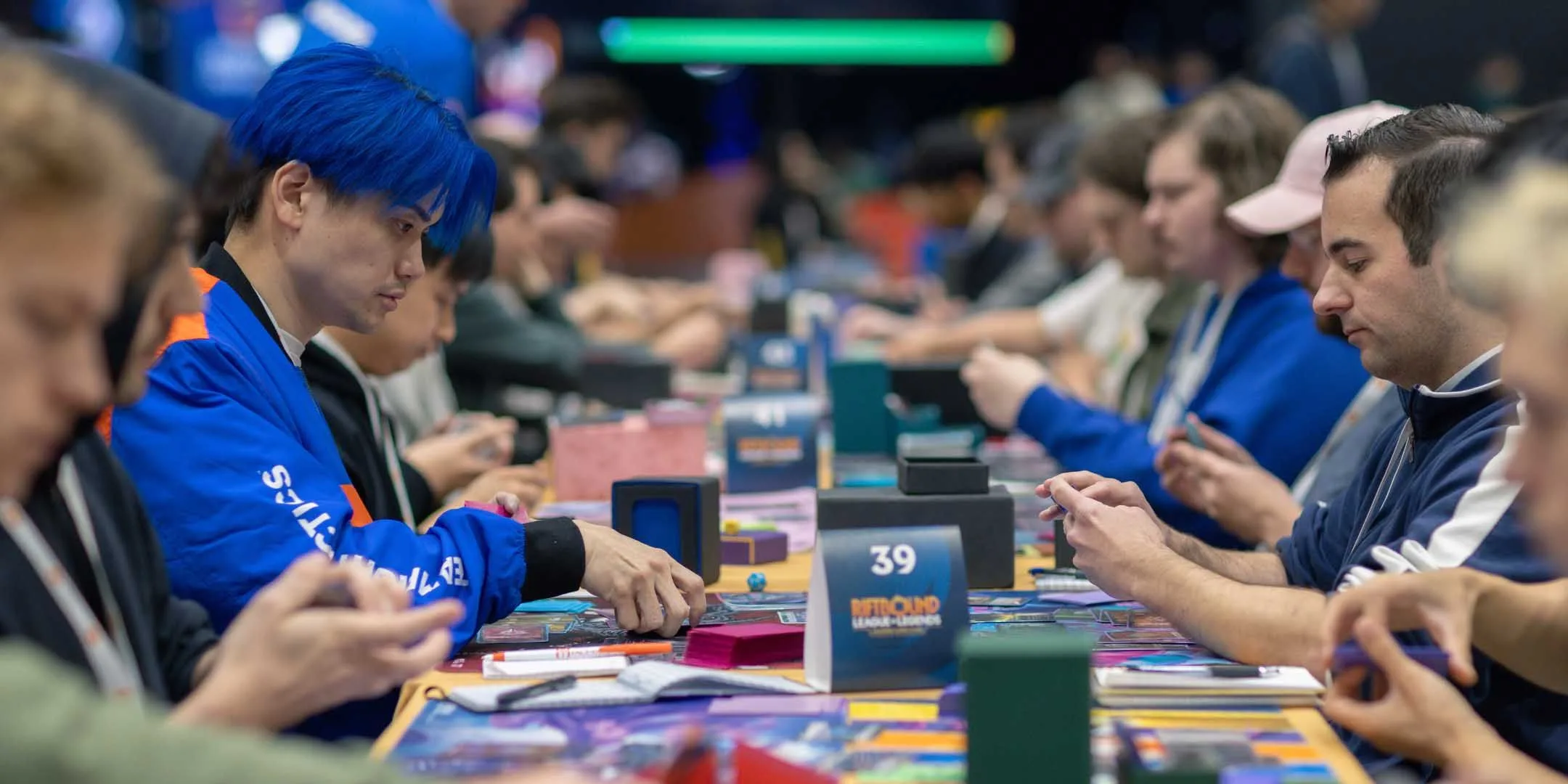 Riftbound players competing at a Regional Qualifier event Riftbound players competing across a long tournament table at a Regional Qualifier event