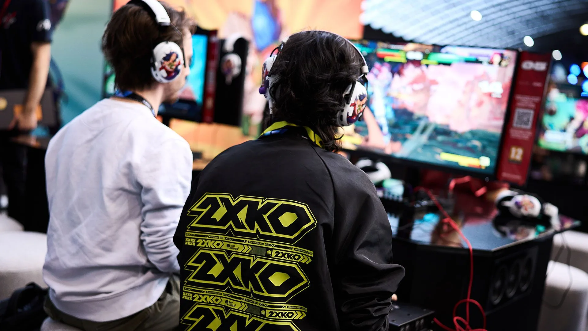 Competitive 2XKO players at an esports tournament Two fighting game competitors wearing headsets at gaming stations during an esports tournament