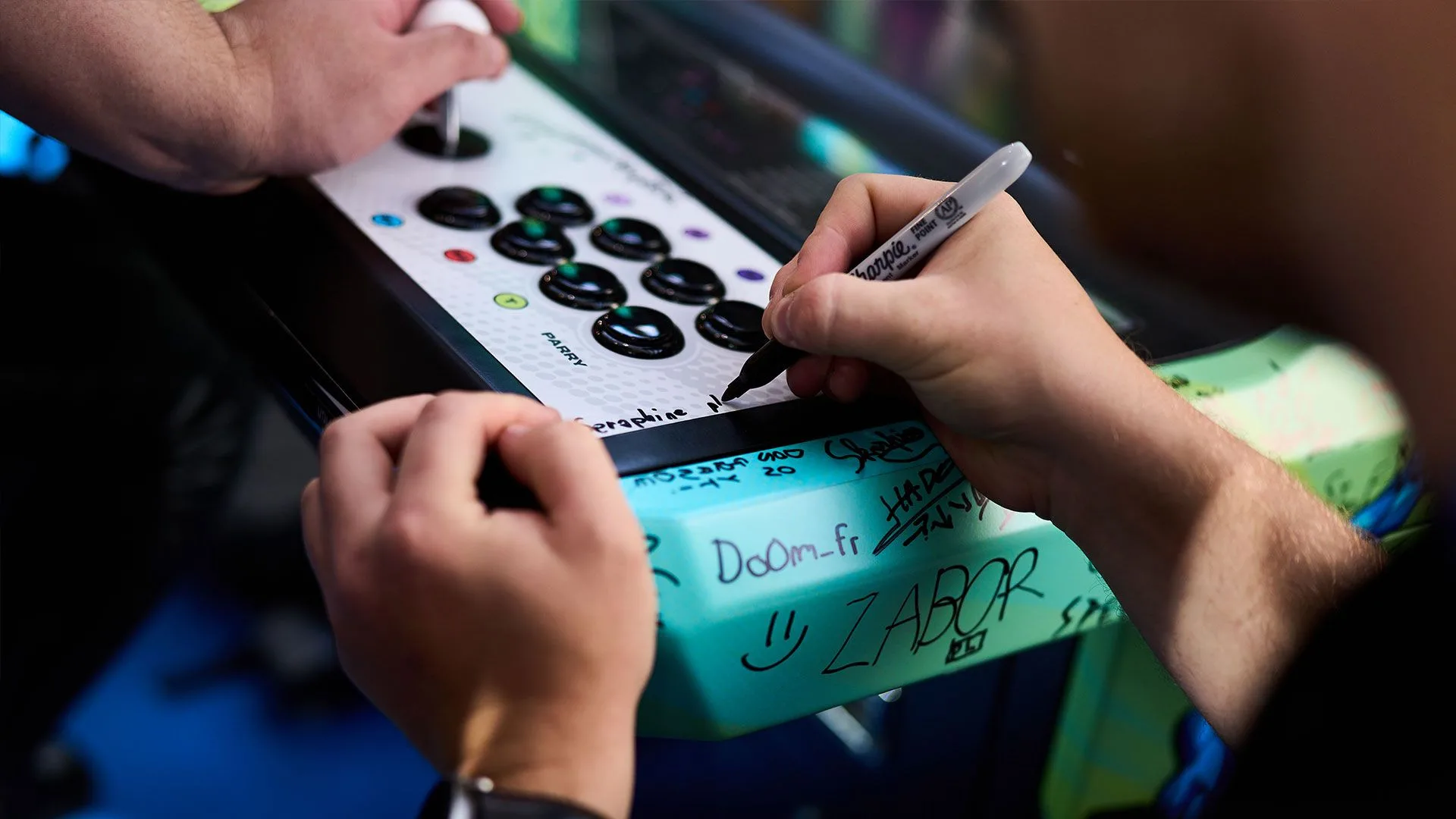 Fighting game community commemorates competitive events with signed arcade controller Person signing a white arcade fighting game controller covered with signatures