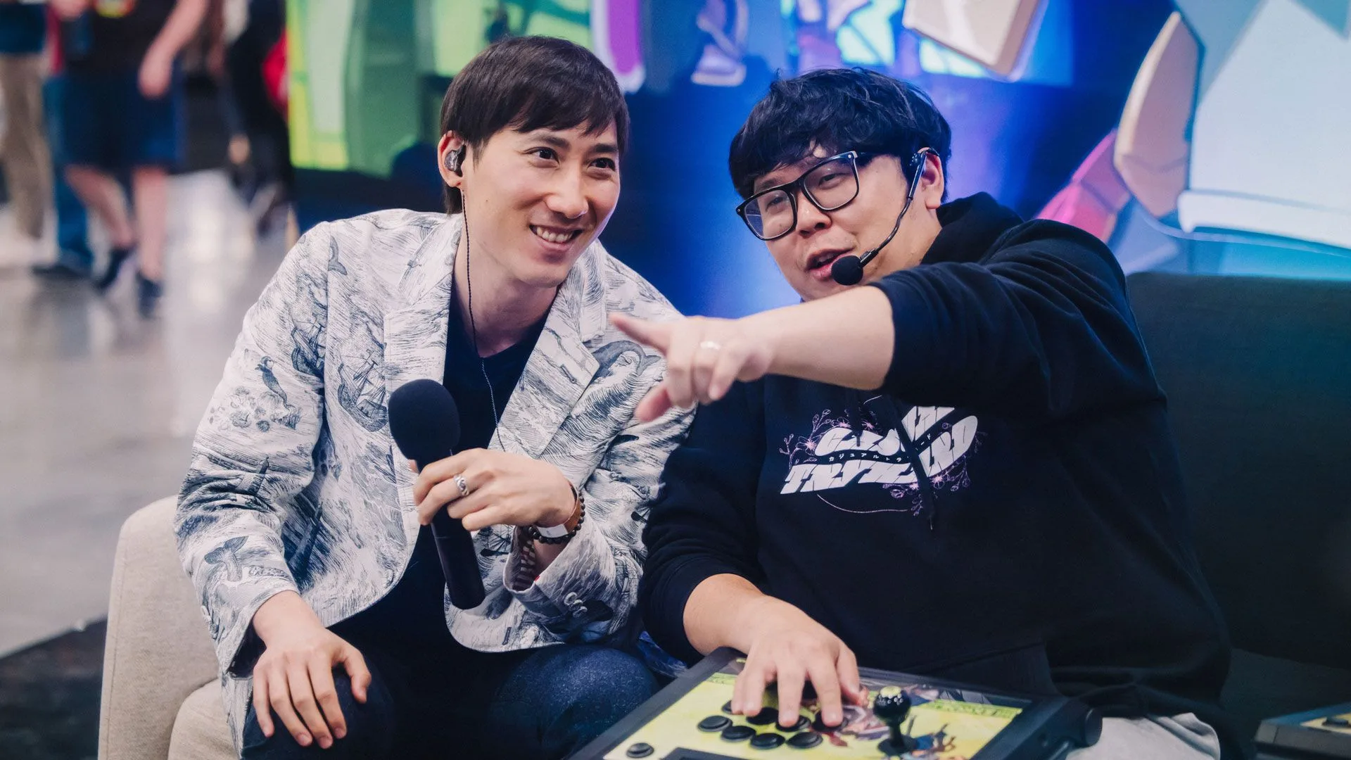 2XKO Evo 2026 broadcast coverage Two 2XKO Evo broadcast personalities sitting near an arcade controller during event coverage